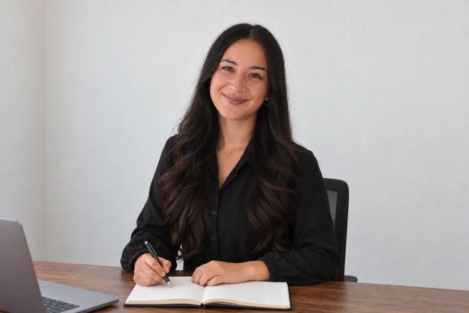 Esra Medik sitzt mit Stift und Notizbuch am Schreibtisch